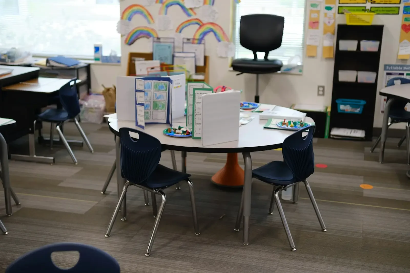 A round table with blue chairs and privacy folders in a classroom